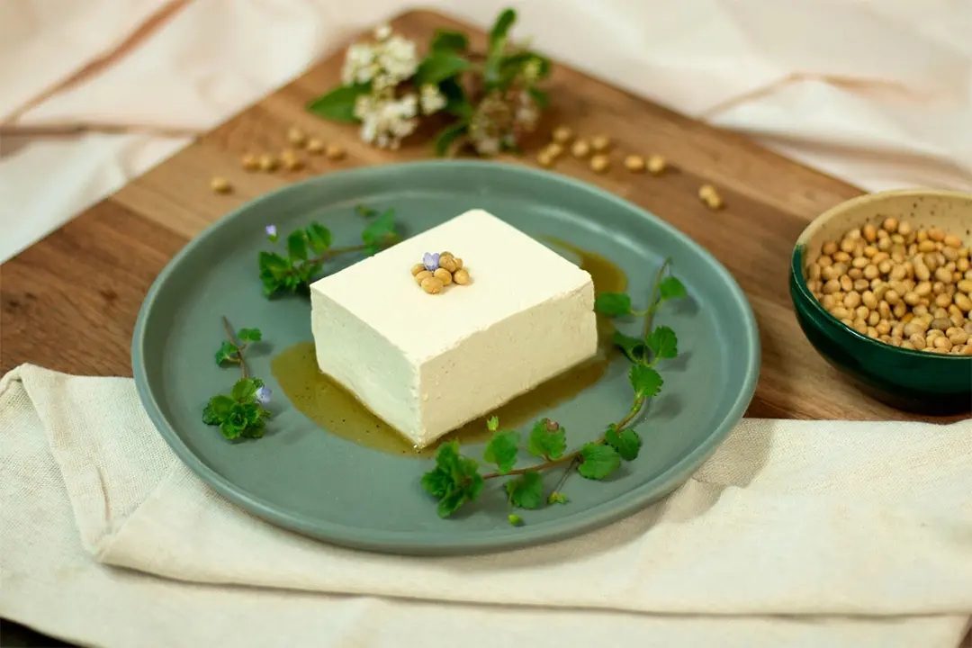 Bloc de tofu nature présenté dans une assiette, décoré avec des fèves de soja et des fleurs