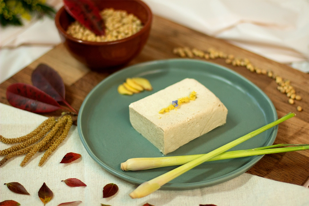 Bloc de tofu au gingembre et à la citronnelle présenté dans une assiette, décoré avec du gingembre haché et des fleurs